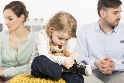 Young family with sad little boy hugging teddy bear and his parents looking depressed