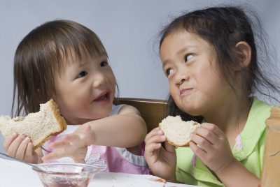 Two sisters making a mess with peanut butter and jelly sandwiches